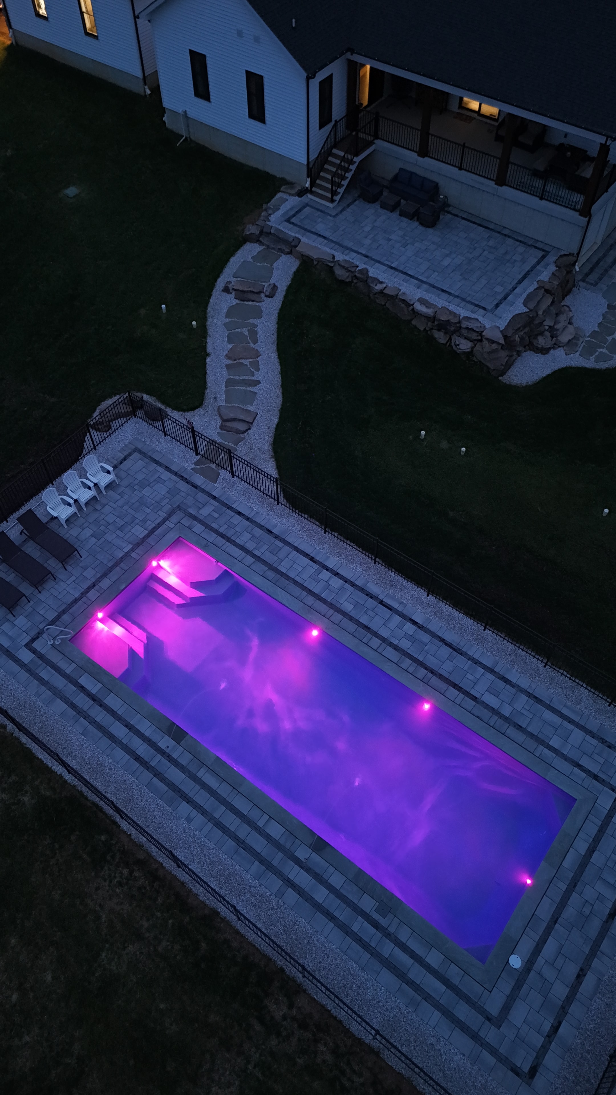 LandPro aerial night shot of pool glowing purple with paver surround, flagstone path, and white gravel