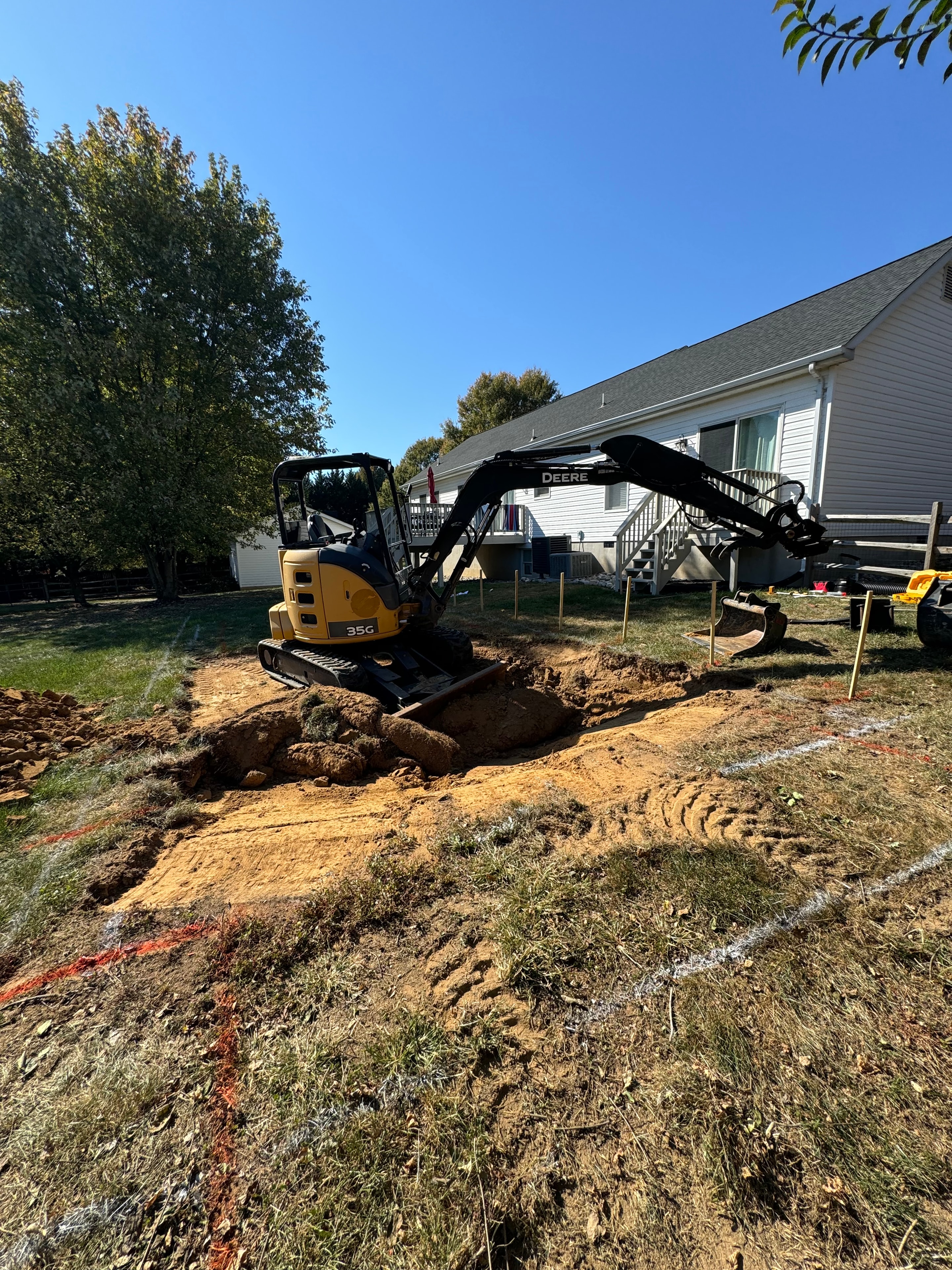 Under construction — excavator digging pool area beside house with stakes and markings