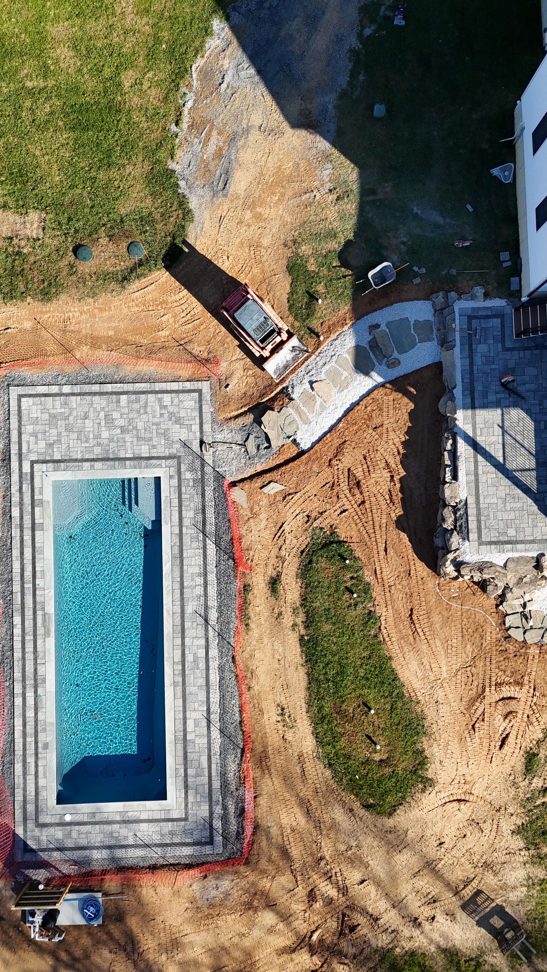 Under construction — aerial view of pool with paver surround and stone path taking shape