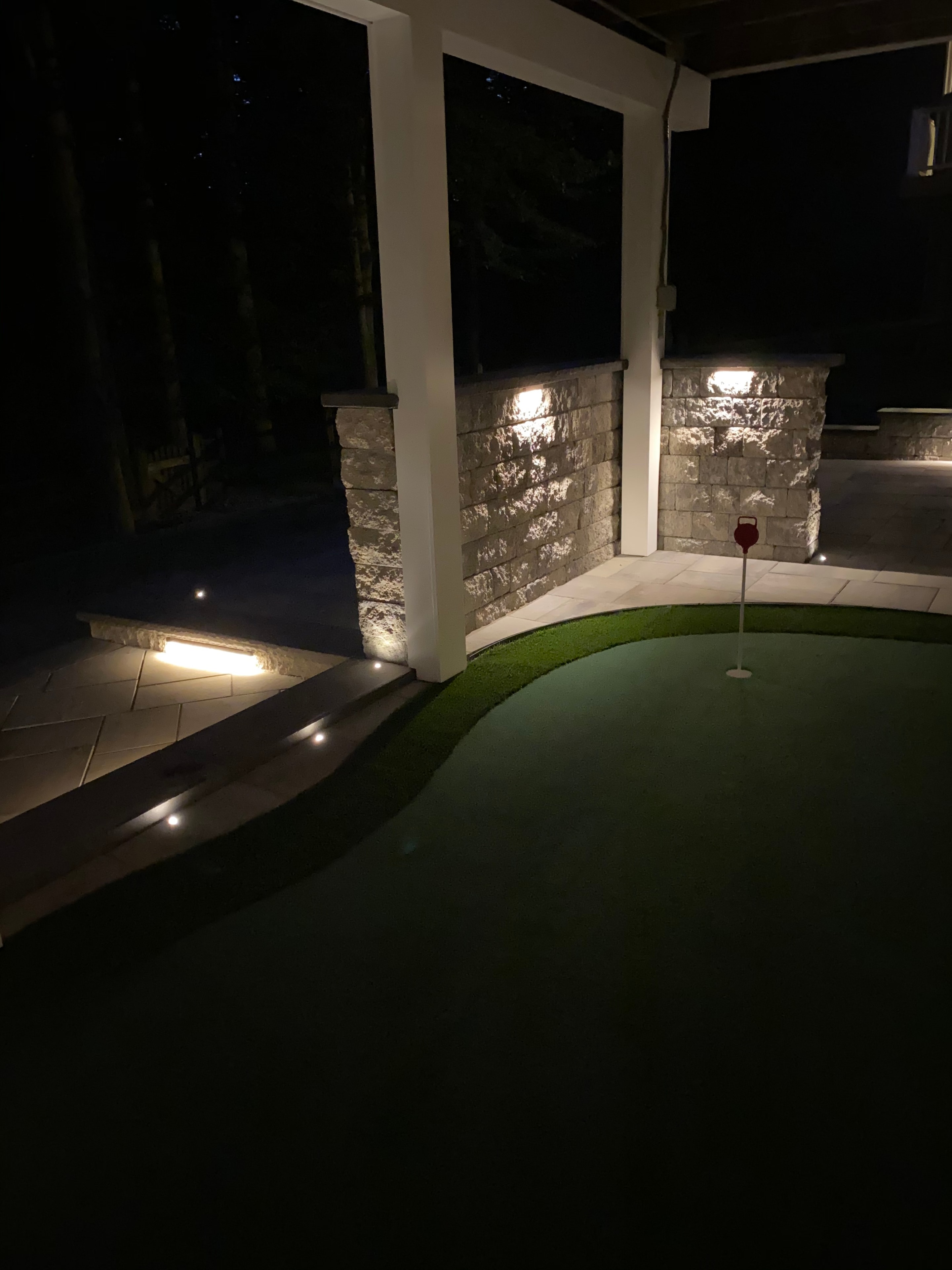 Golfing Paradise — dark nighttime shot of putting green with red flag, paver steps, and warm LED accent lighting