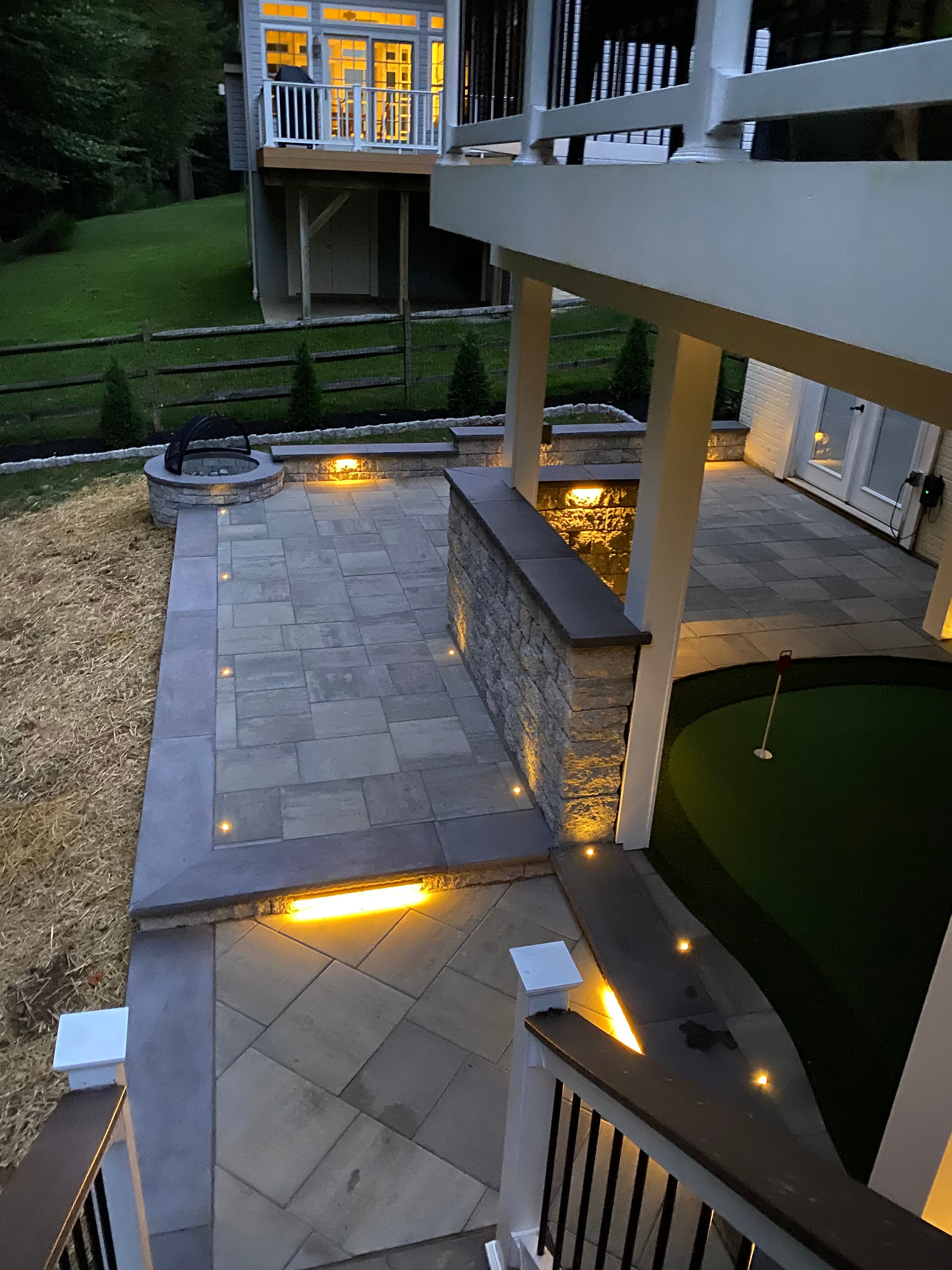 Golfing Paradise — evening shot of paver patio with LED lighting, granite sitting wall, and putting green glowing in background