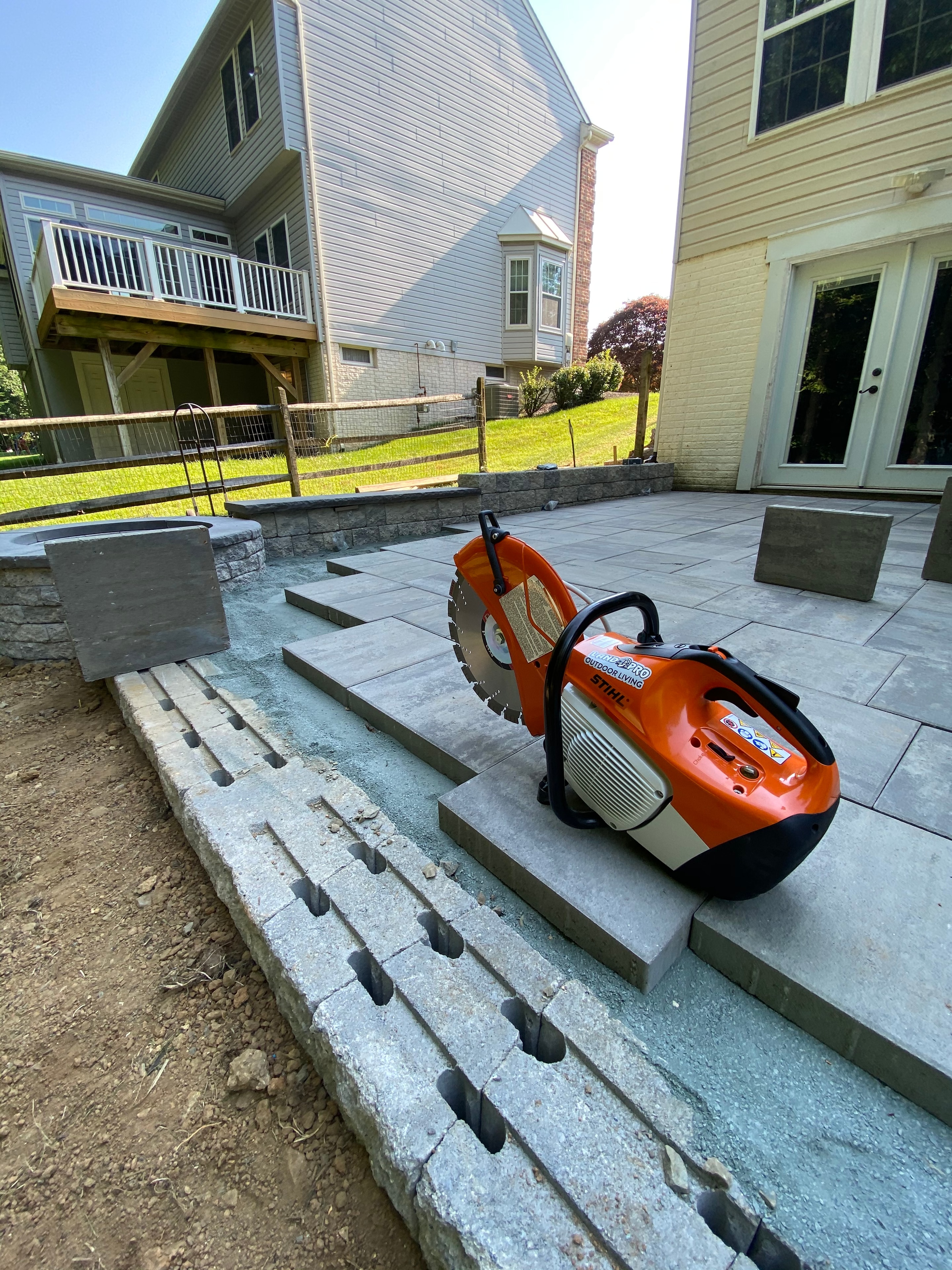 Under construction — Stihl cut-off saw resting on partially laid paver patio with sitting wall in progress