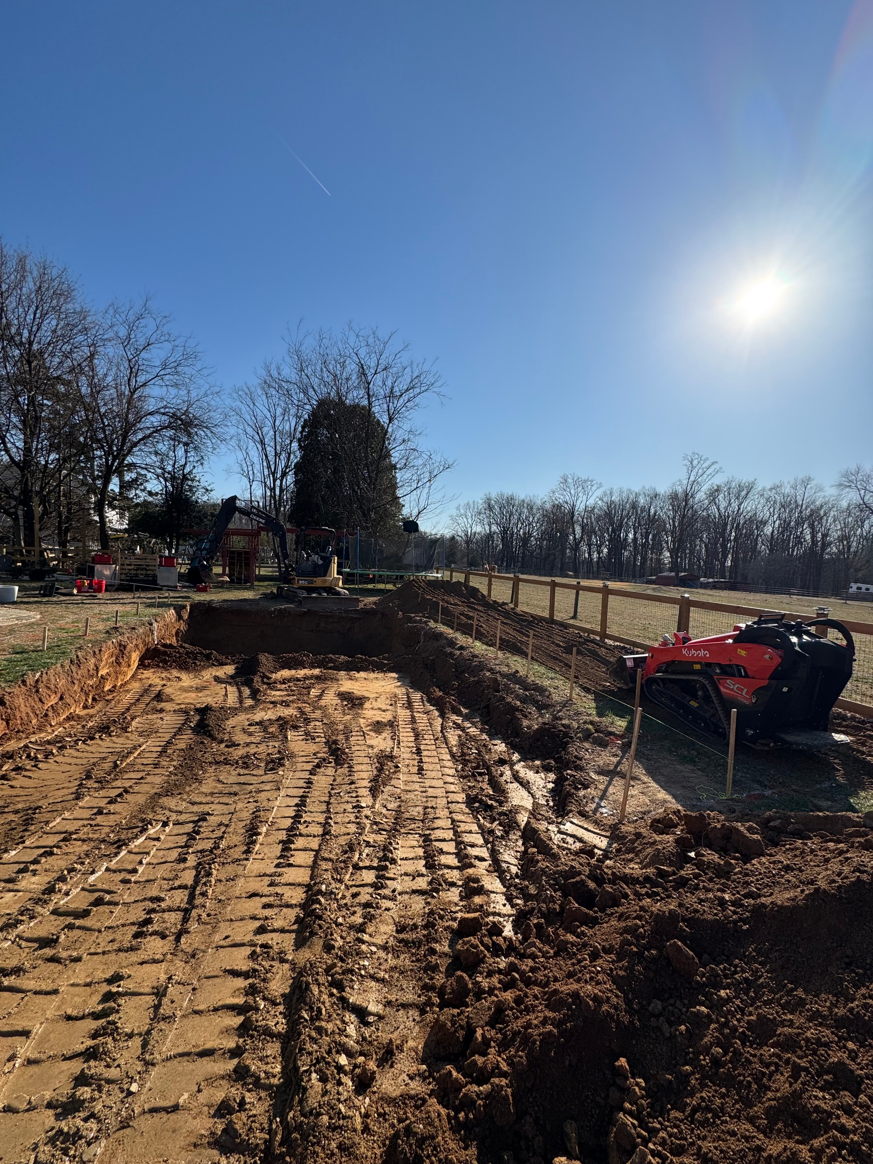 Under construction — Kubota excavator digging pool area with fresh earth mounded beside trench