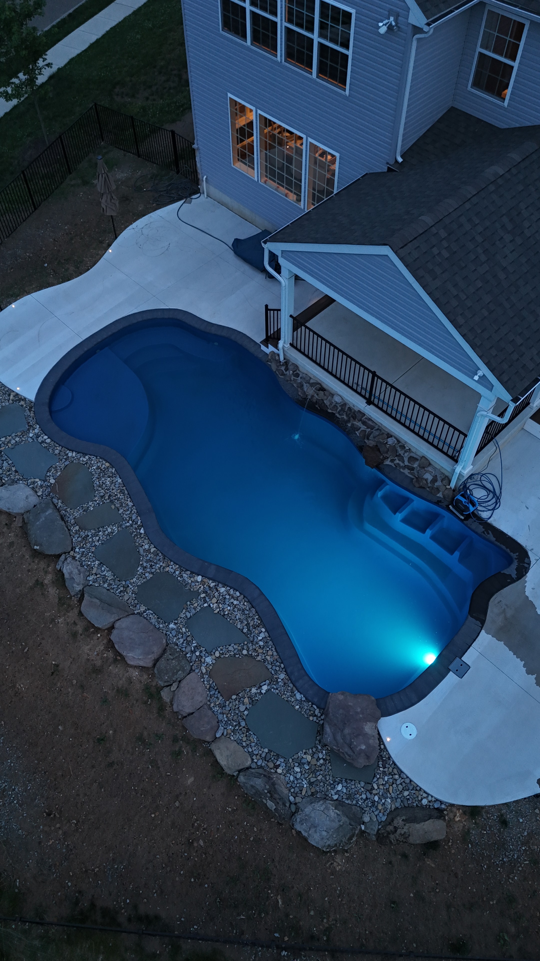 Tight Quarters — aerial dusk shot of pool with blue LED light glowing, concrete patio, and pergola